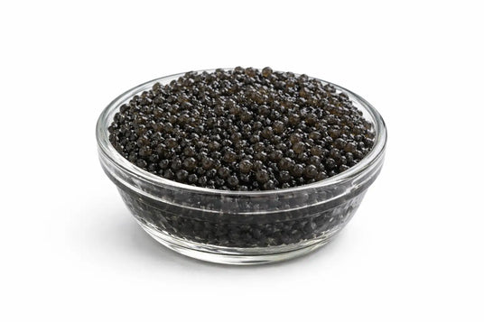 Un bol de vidrio transparente lleno de caviar negro.