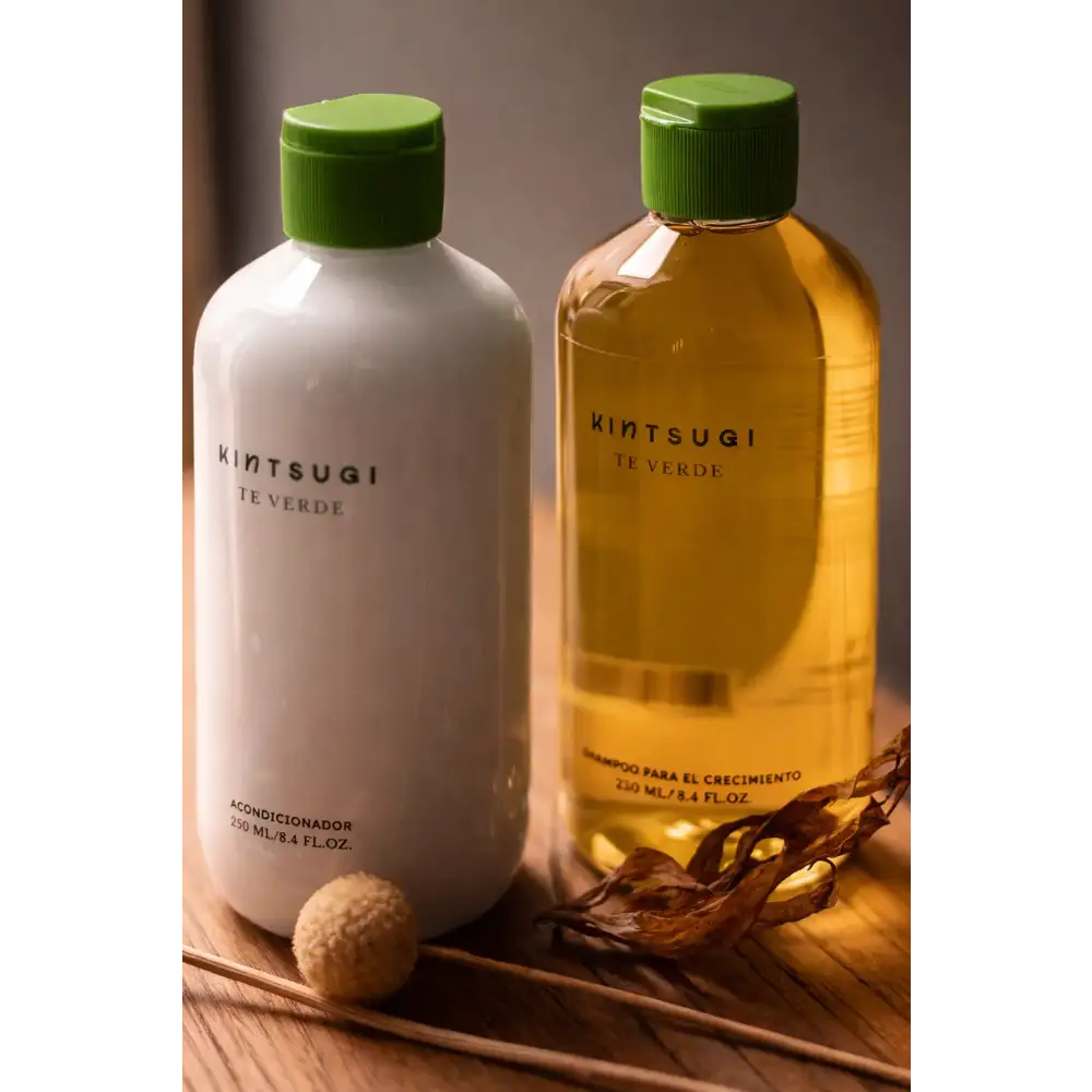 Dos botellas de kintsugi te verde, una blanca con tapa verde que contiene acondicionador y la otra botella transparente ámbar con tapa verde a juego que contiene champú para el crecimiento del cabello.