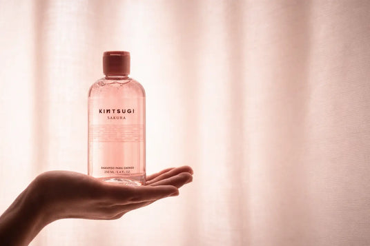 Una botella translúcida rosa de champú kintsugi sakura para niños, sostenida en una mano.