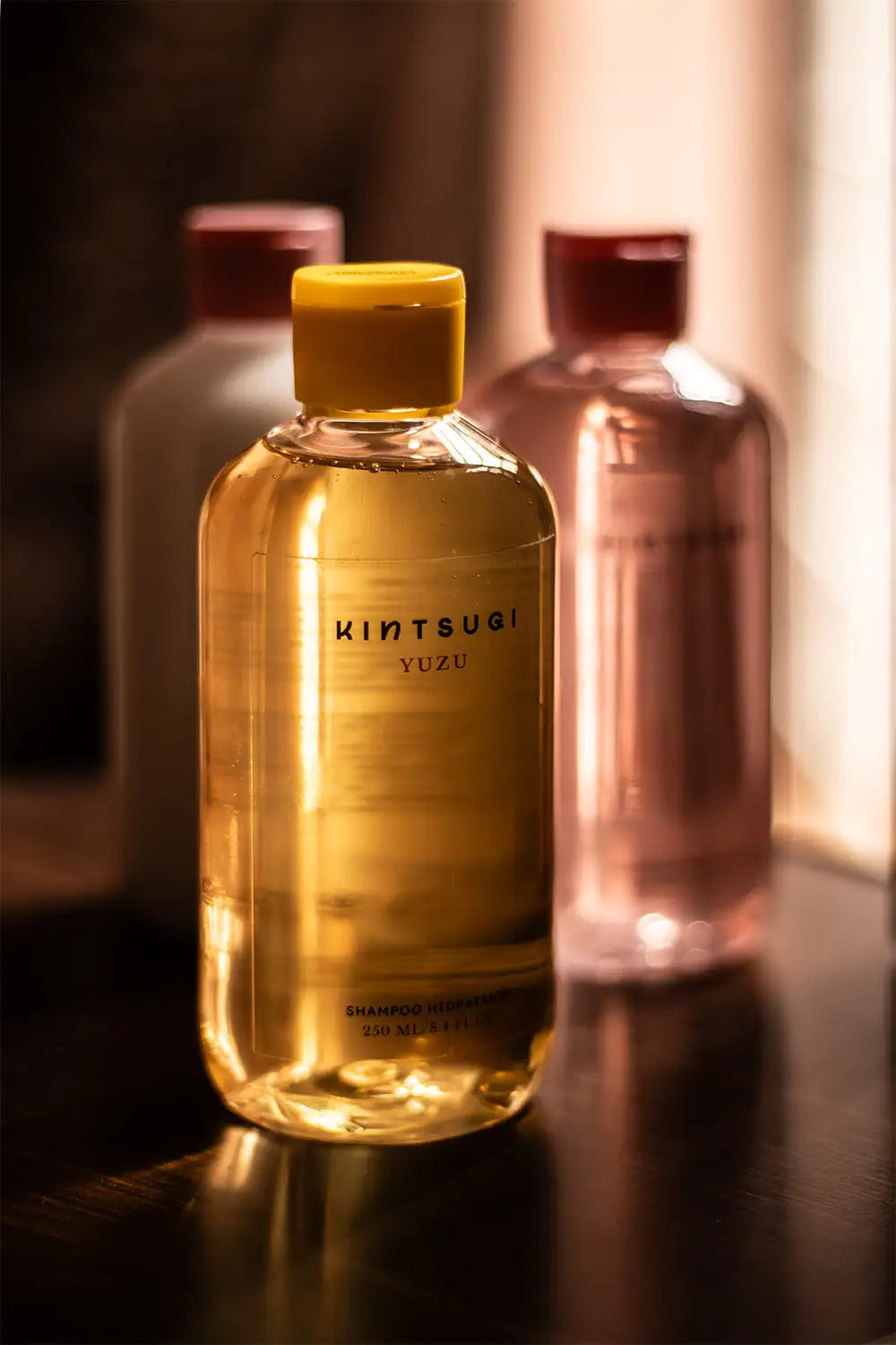 Una botella de vidrio transparente con tapa amarilla que contiene champú de yuzu kintsugi de tono dorado, etiquetado como 250 ml.